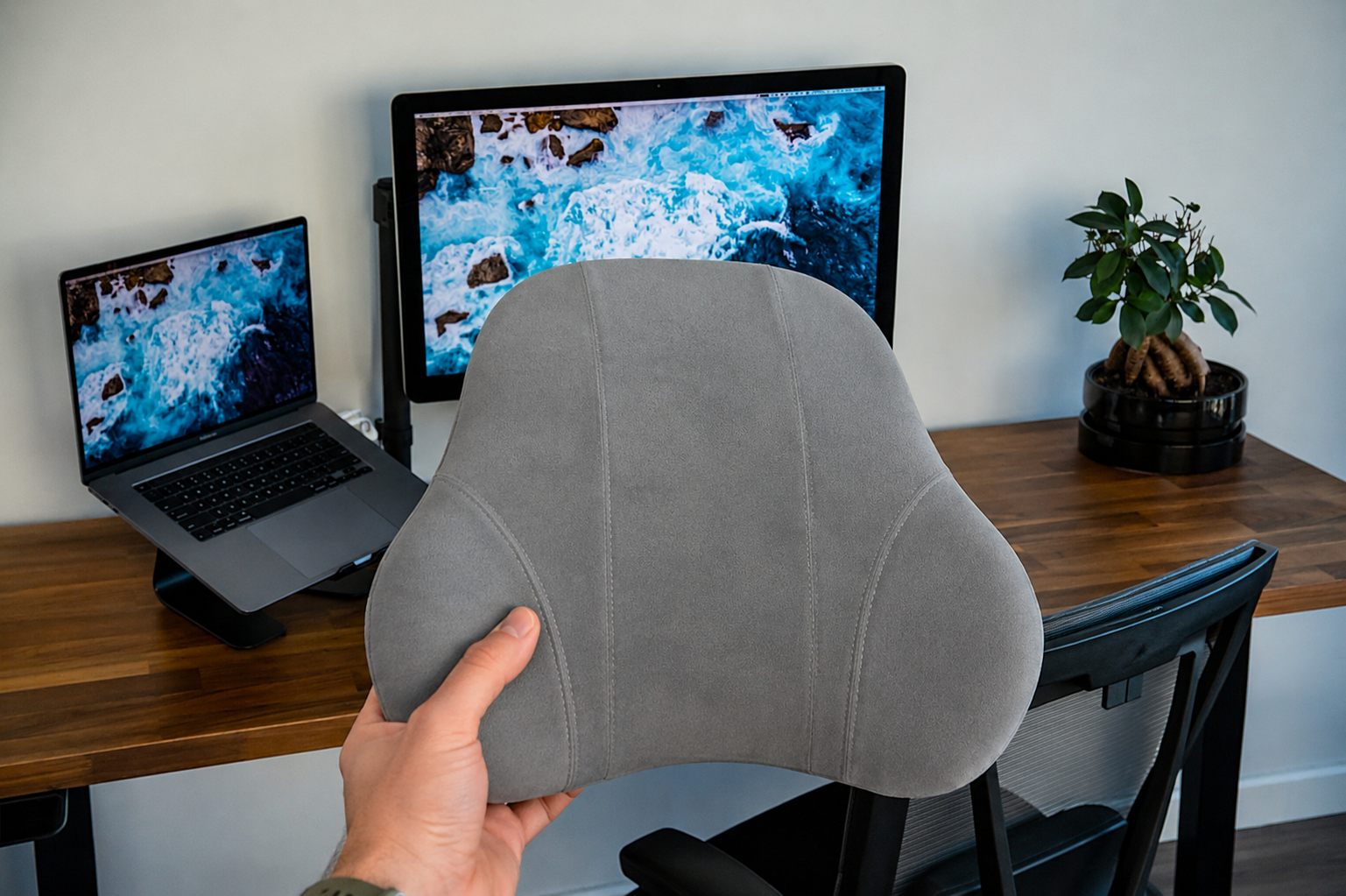 BackMod lumbar cushion held up at a clean desk setup